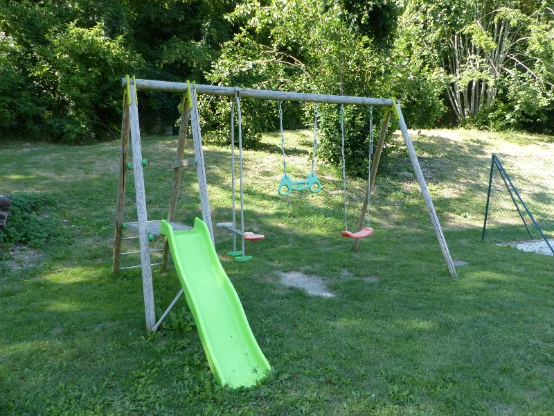 Aire de jeux avec toboggan vert et balançoires dans un grand jardin arboré
