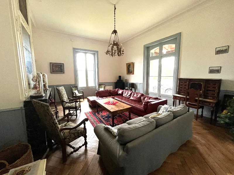 Grand salon avec parquet, canapés en cuir rouge, lustres et mobilier ancien