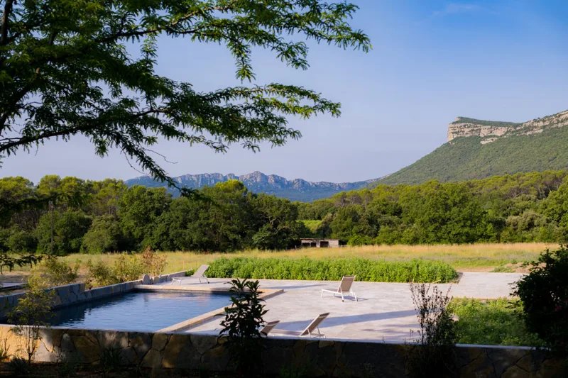 Grande piscine extérieure ouverte sur un paysage de garrigue et de reliefs montagneux
