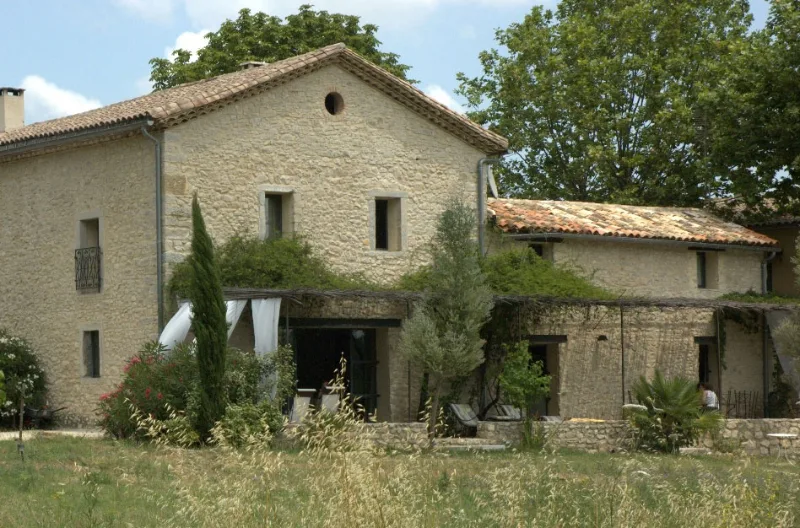 Façade en pierre du mas provençal entourée d'arbres et de végétation sous ciel dégagé
