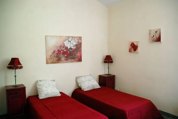 Chambre épurée avec deux lits simples habillés de rouge, chevets et tableaux floraux