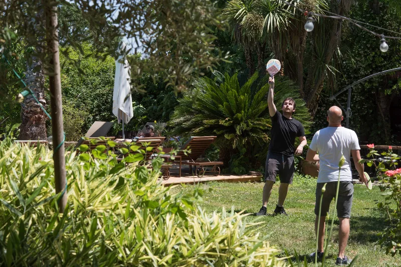 Jardin arboré ensoleillé où des participants jouent au ballon près d'une terrasse en bois