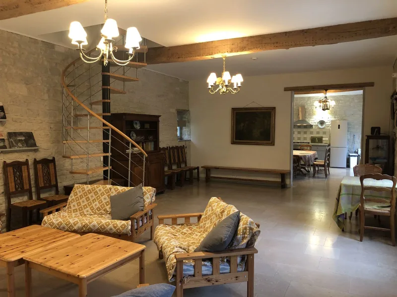 Salon lumineux du gîte principal avec mobilier confortable, escalier en colimaçon et accès aux chambres