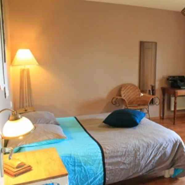 Chambre avec lit double, couvre-lit bleu canard et lampe de chevet allumée