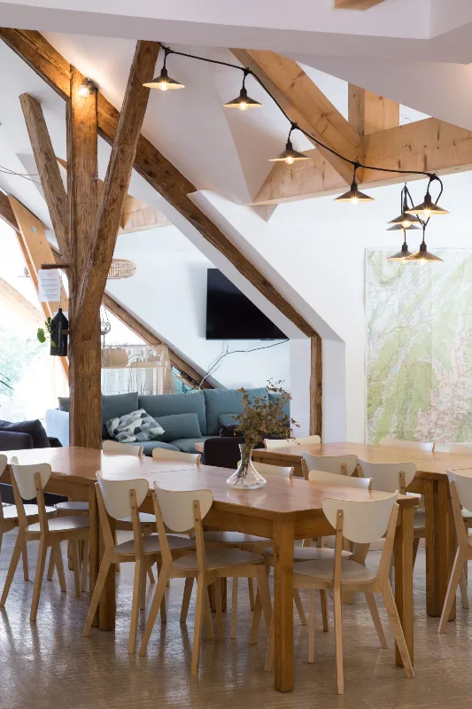 Salle à manger sous charpente avec tables en bois et guirlandes lumineuses
