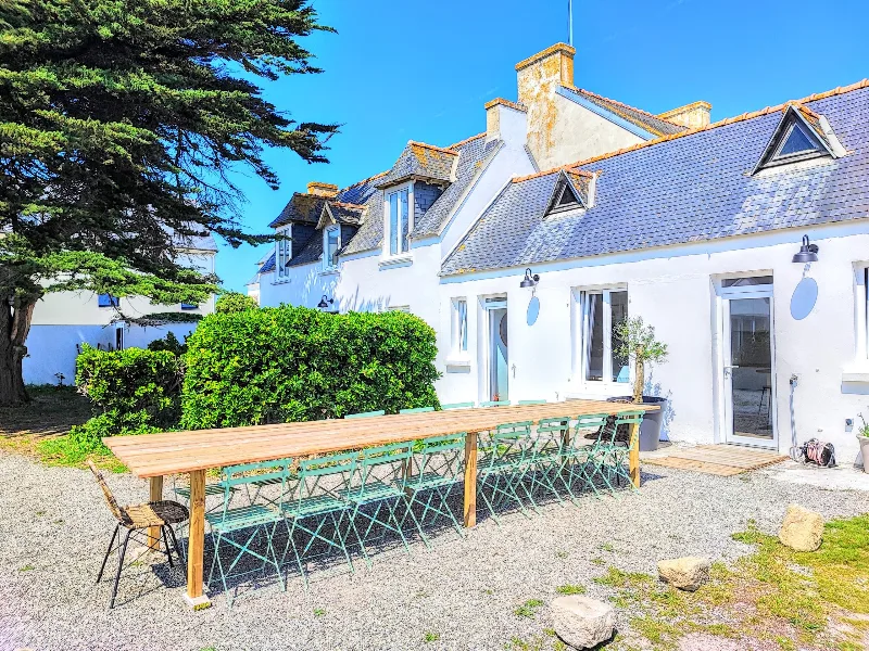 Terrasse extérieure avec longue table en bois pour 15 convives devant la façade du gîte, ciel breton bleu