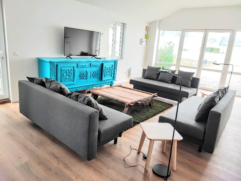 Grand salon annexe de 60 m² avec trois canapés gris, bahut turquoise et baies vitrées lumineuses