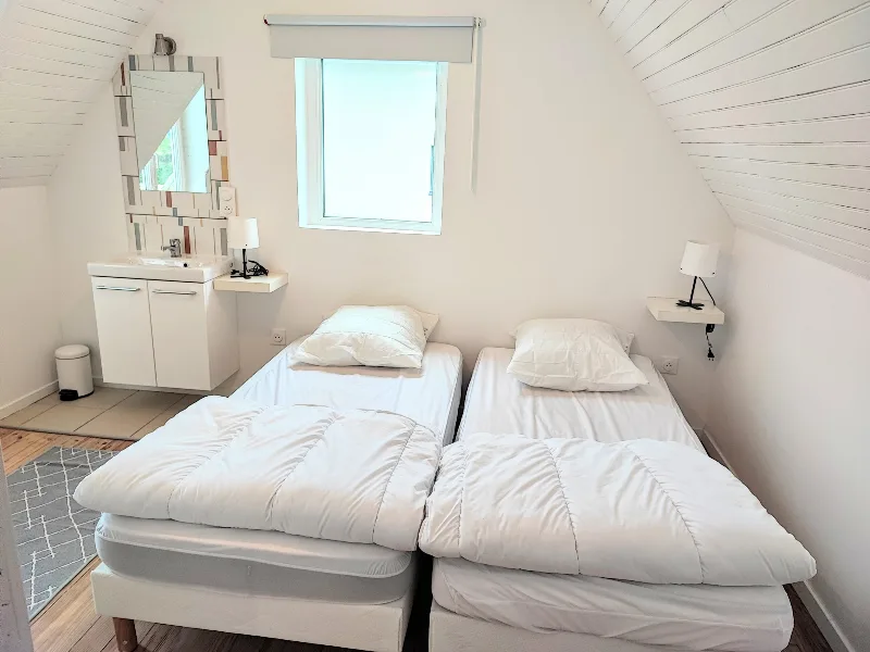 Chambre mansardée avec deux lits simples, lavabo intégré, décor épuré en blanc et parquet