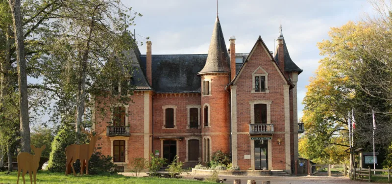 Façade château en brique avec tourelle centrale et parc arboré en automne