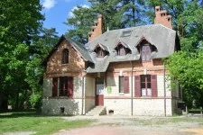 Maison forestière en pierre avec volets rouges entourée d'arbres en été