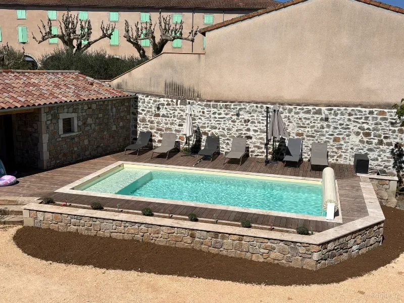 Piscine chauffée avec transats de La Maison des Papés, entourée de pierres et avec la bâtisse ardéchoise en arrière-plan