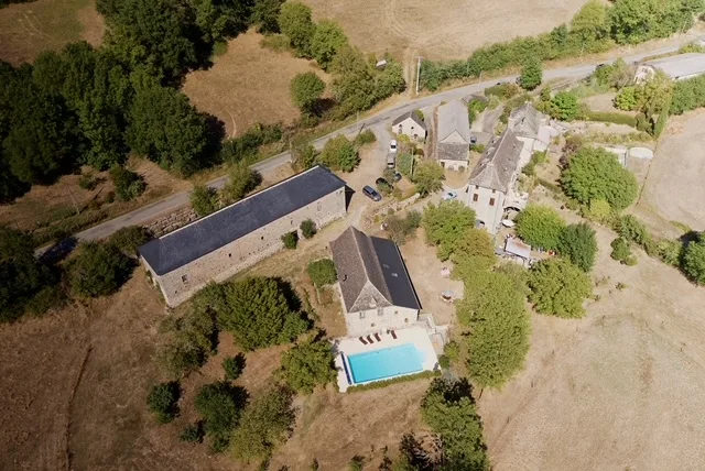 Vue aérienne du domaine avec manoir en pierre, gîte et piscine entourés de collines aveyronnaises
