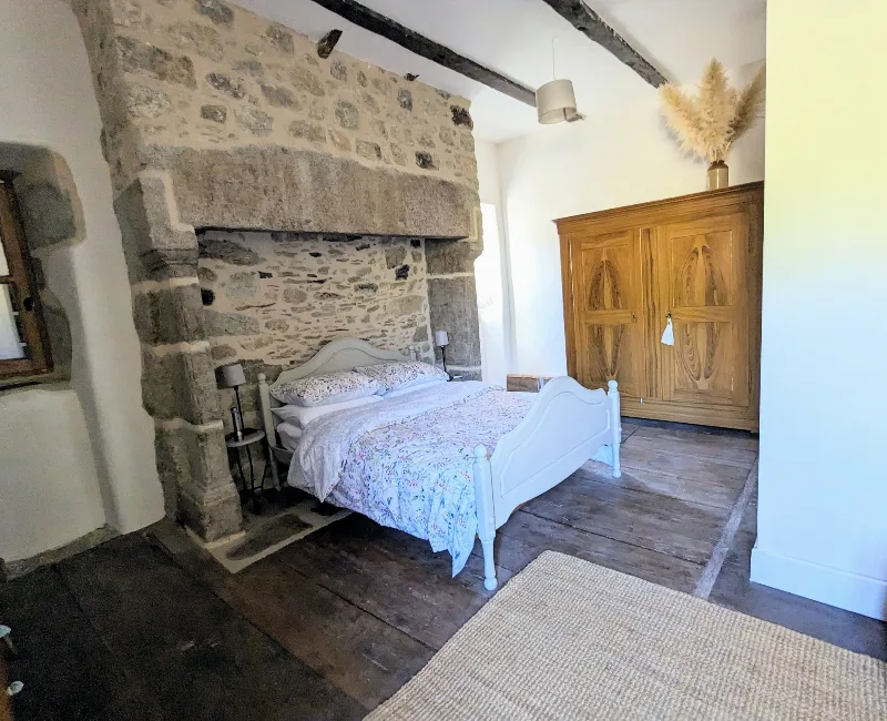Chambre principale du manoir avec lit double, alcôve en pierre et parquet ancien