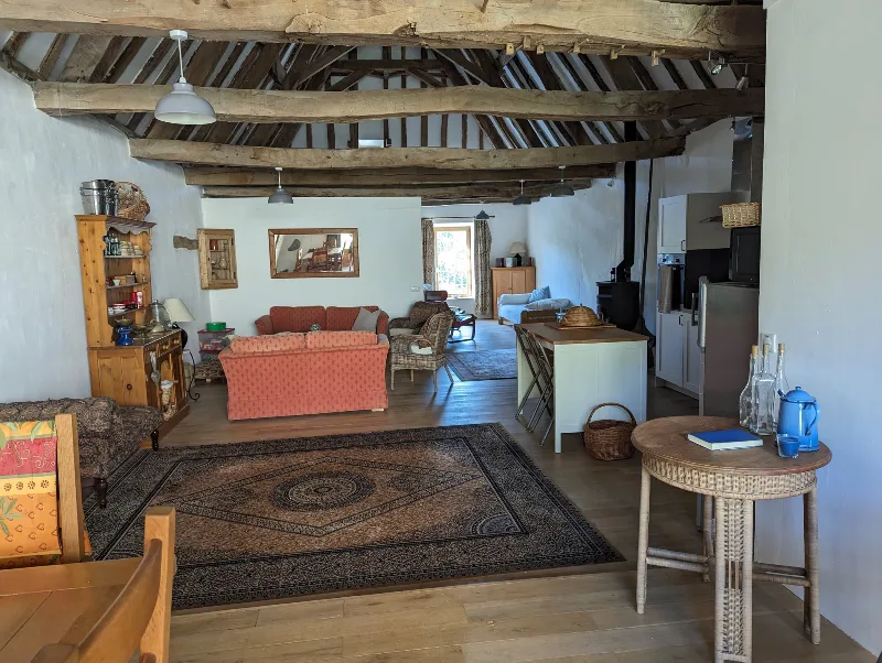 Grand salon ouvert avec poutres apparentes, canapés et coin cuisine du gîte La Châtaigne