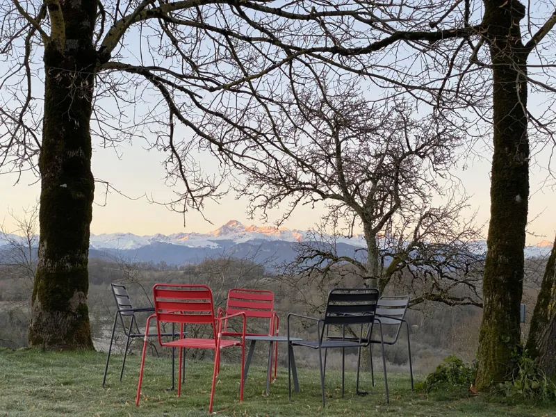 Chaises de jardin sous des arbres nus avec vue sur les Pyrénées enneigées