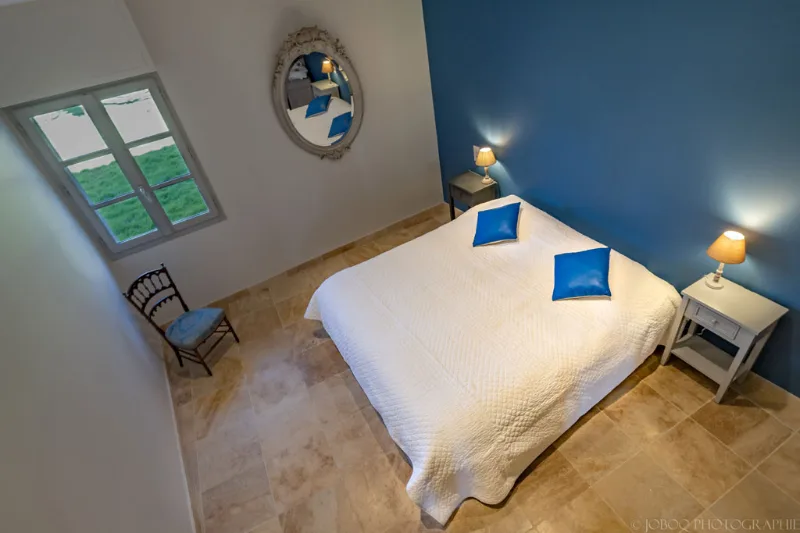 Chambre bleue avec grand lit blanc, miroir baroque et sol en pierre naturelle