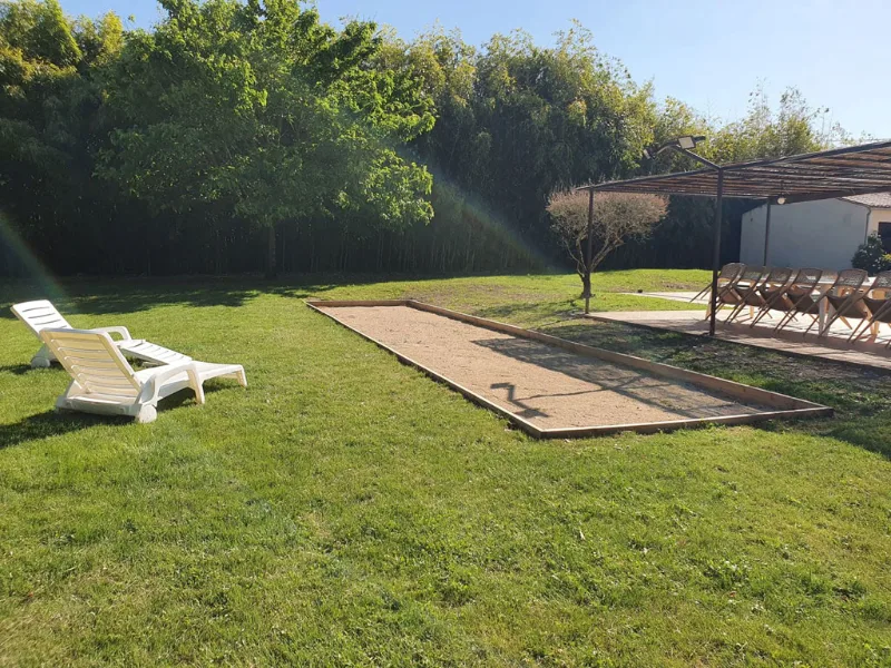 Terrain de pétanque sur pelouse avec transat blanc et pergola en fond