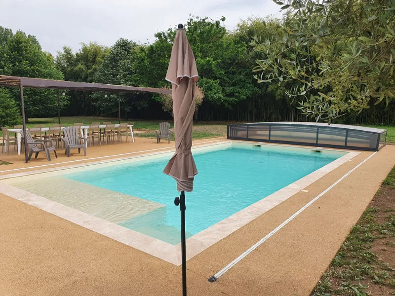 Piscine avec abri semi-ouvert, parasol et transats sur pelouse