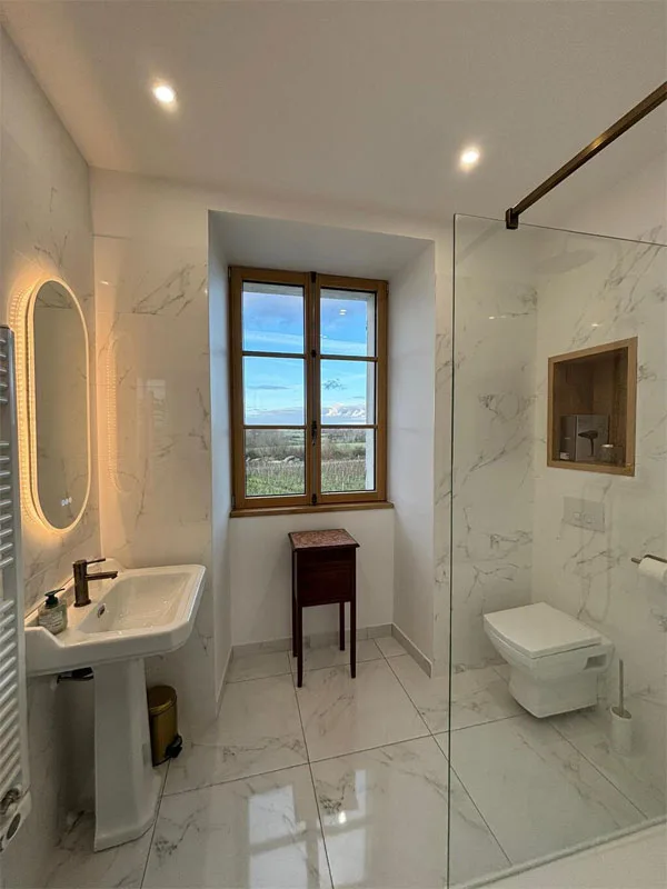 Salle de bain en marbre blanc avec douche à l'italienne et fenêtre sur vignes
