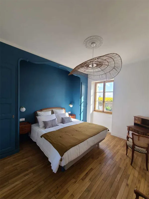Chambre bleue avec grand lit, suspension en rotin et parquet en chêne