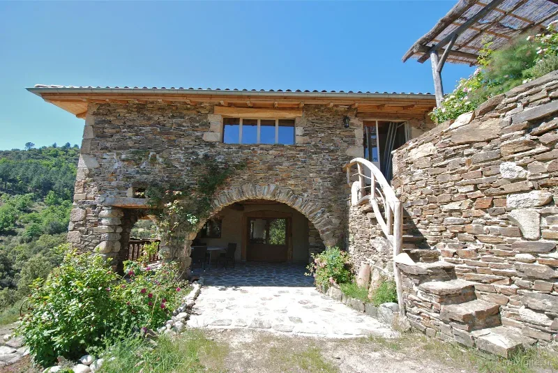 Bâtisse en pierre sèche avec arche voûtée et escalier extérieur sur fond boisé