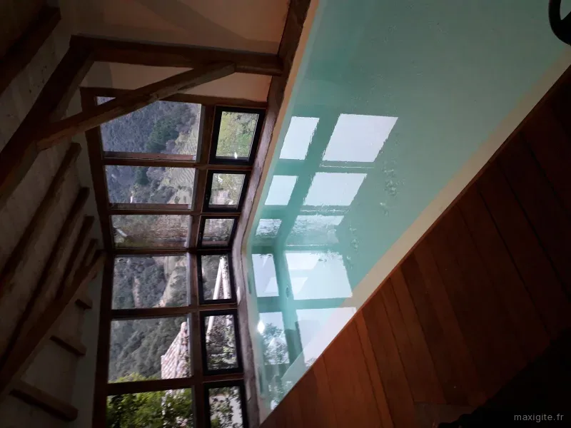 Piscine intérieure sous charpente bois avec verrière et vue sur vallon boisé