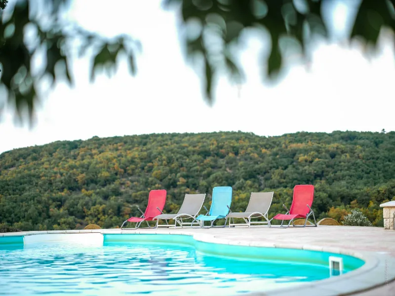 Transats rouges et bleus au bord d'une piscine avec vue sur colline boisée