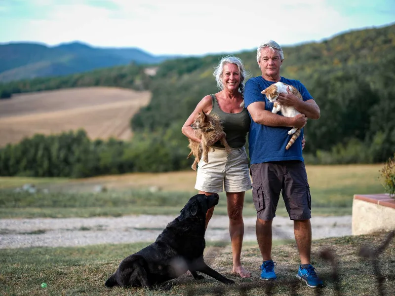 Couple d'hébergeurs avec chiens et chat devant panorama de collines