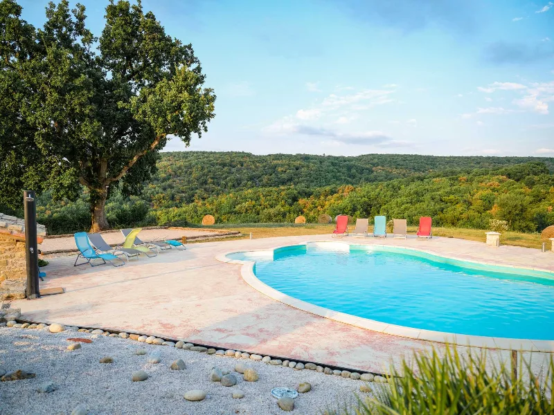 Piscine ronde avec transats colorés et vue panoramique sur vallée boisée