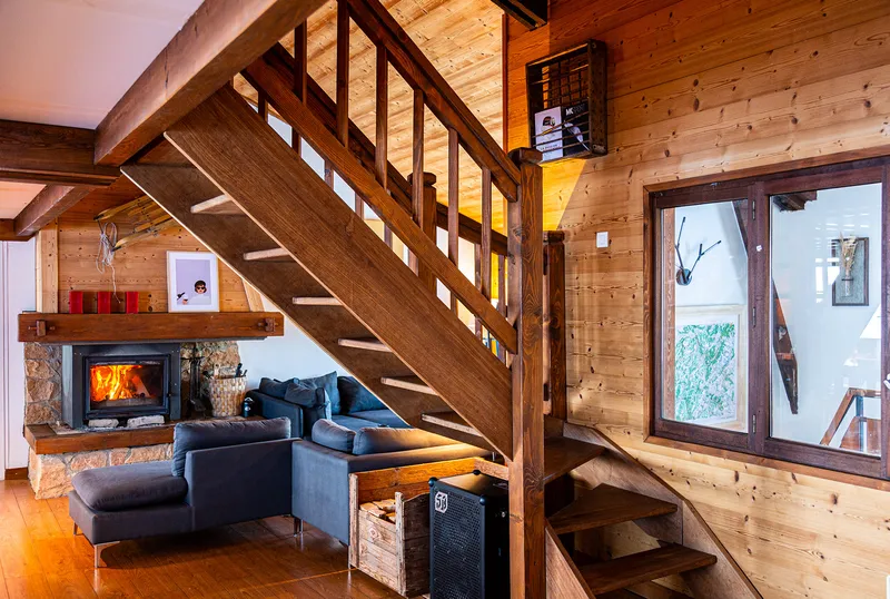 Grand salon du chalet avec cheminée en pierre et canapés face aux baies vitrées sur la montagne