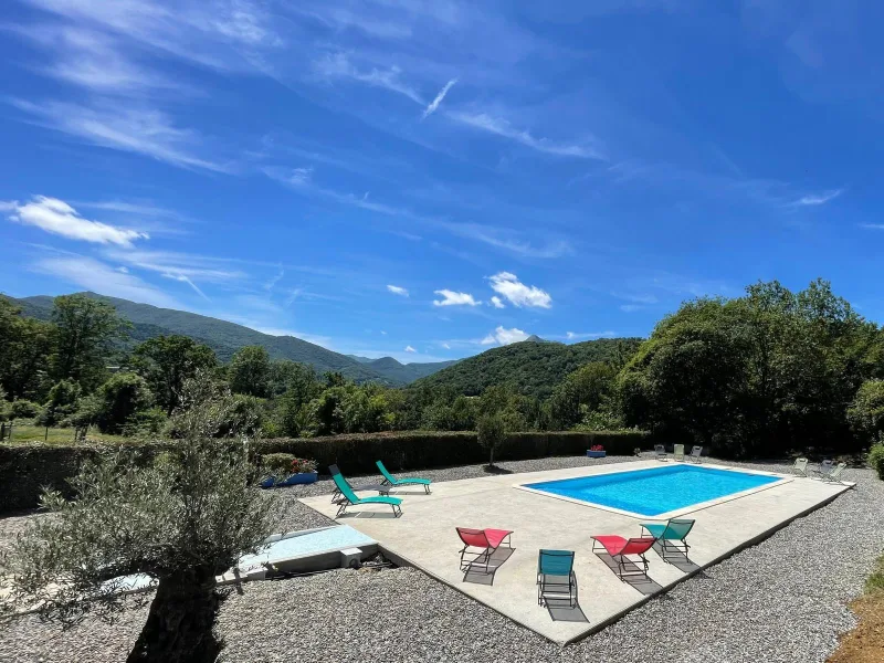 Piscine rectangulaire avec transats colorés et vue panoramique sur montagnes boisées