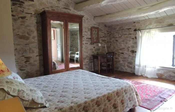 Chambre mansardée aux murs en pierre apparente avec armoire ancienne en bois et lit fleuri