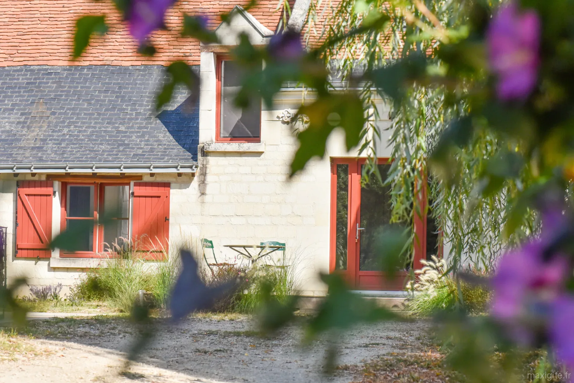 Gîte de groupe La Maison de Thélème à Huismes — Longère en tuffeau aux volets rouges, avec porte vitrée ouverte sur la cour du domaine viticole, capacité 12 personnes