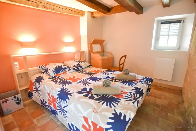 Chambre corail avec lit à motifs fleuris, coiffeuse en bois et fenêtre sous poutres apparentes