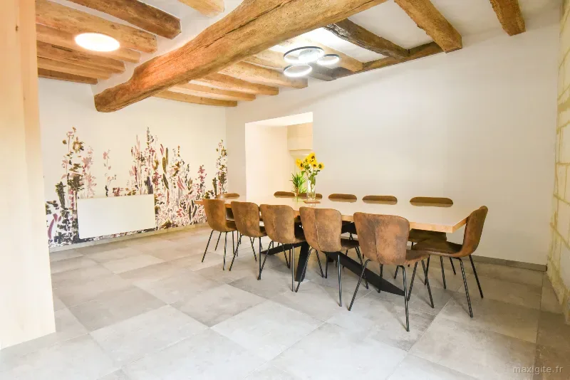 Grande salle à manger aux poutres apparentes avec table en bois pour dix convives