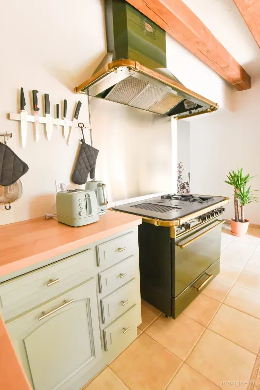 Cuisine avec piano de cuisson en laiton et hotte cuivrée sous une poutre ancienne