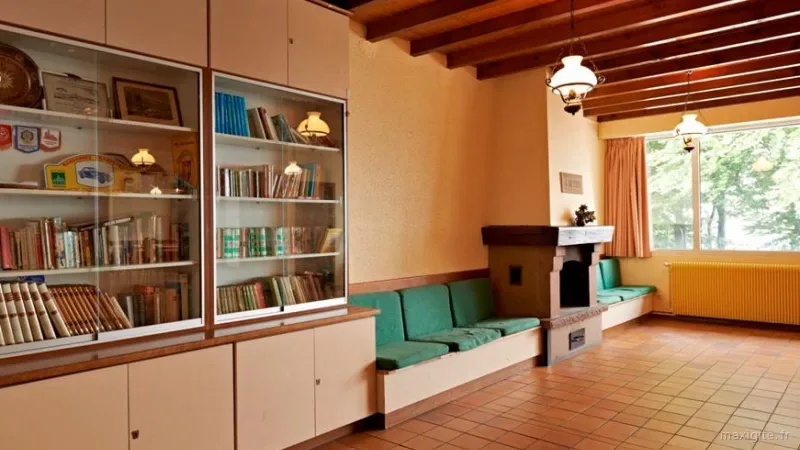 Coin salon avec cheminée en pierre, banquettes vertes et bibliothèque vitrée, espace détente du gîte