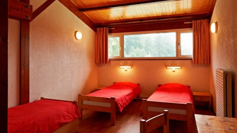 Chambre à trois lits simples avec parures rouges, boiseries et grande fenêtre donnant sur la forêt