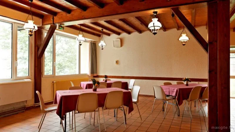 Salle à manger commune aux poutres apparentes, tables dressées et suspensions lumineuses façon lanterne