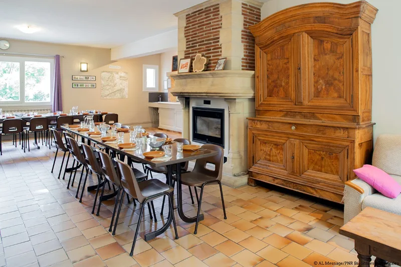 Salle à manger commune avec cheminée en pierre, armoire ancienne et tables dressées pour le groupe