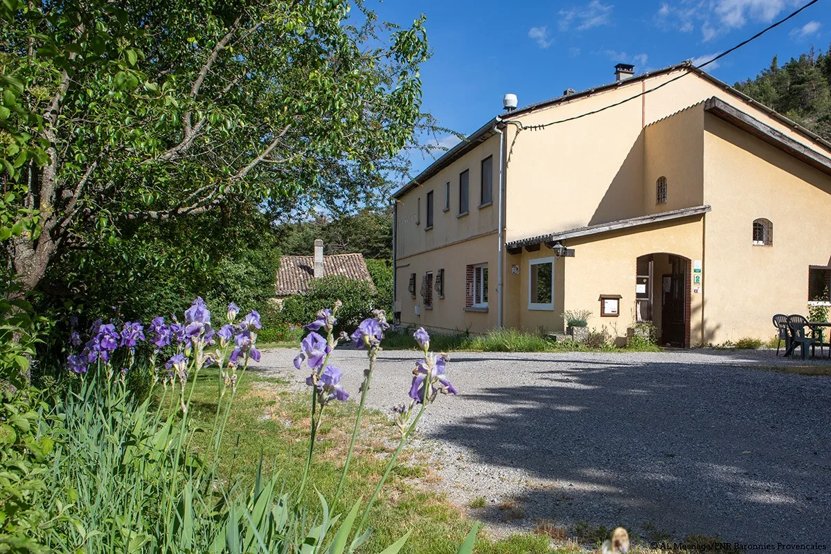 Gîte de groupe Gîte du Mont-Garde à Trescléoux — Façade ocre du Gîte du Mont-Garde à Trescléoux, entourée d'iris et de verdure, sous le soleil des Hautes-Alpes, capacité 38 personnes
