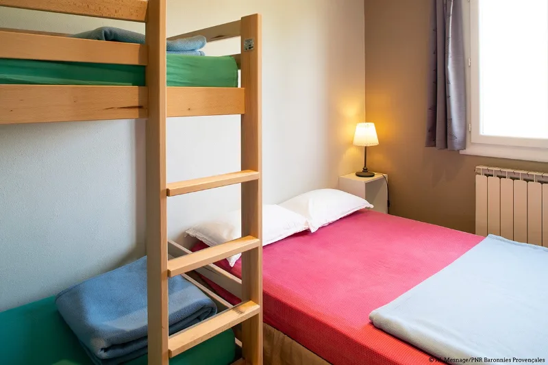 Chambre avec lits superposés et lit double aux parures colorées, ambiance chaleureuse en soirée
