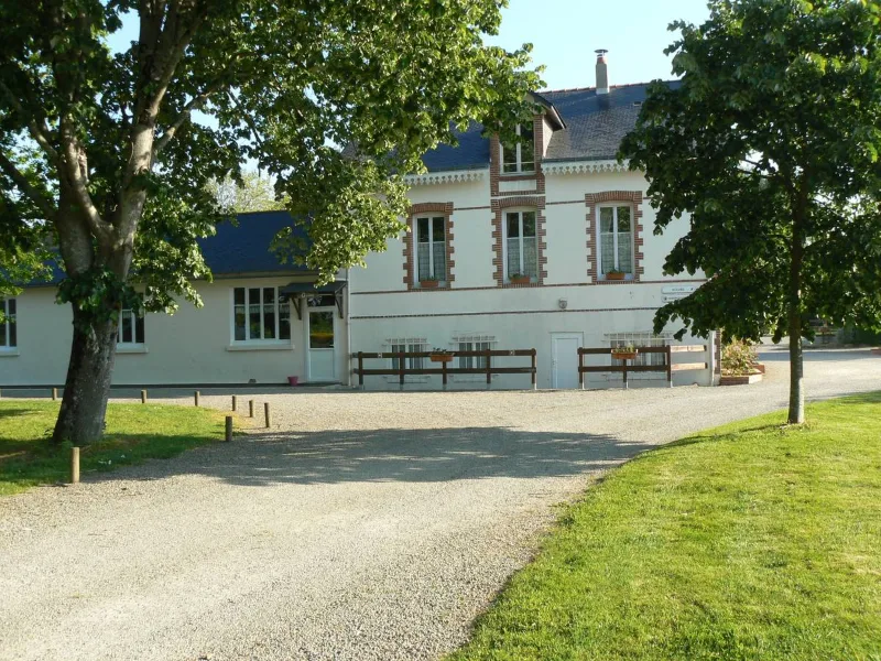 Maison bourgeoise blanche avec allée de gravier et pelouse arborée sous ciel bleu