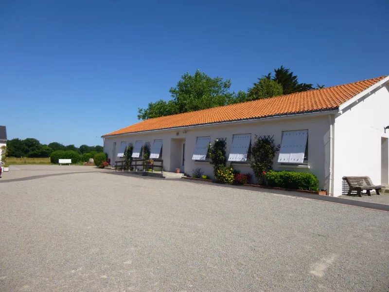 Bâtiment blanc de plain-pied avec toit orangé, jardinières fleuries et vaste parking