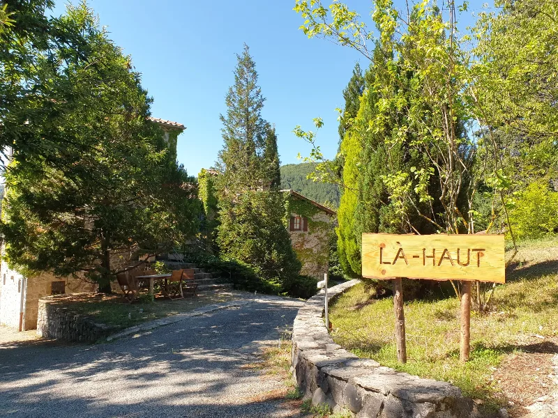 Allée d'entrée bordée de cyprès avec le panneau en bois gravé « Là-Haut »