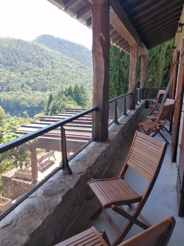 Long balcon de pierre en surplomb de la vallée boisée, chaises en bois pour profiter du panorama