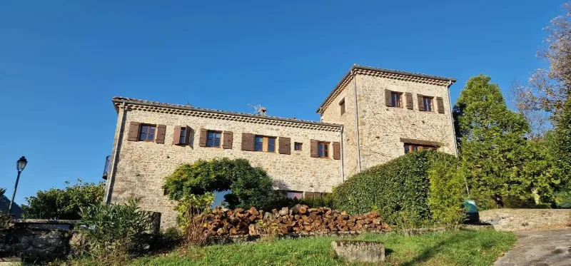 Façade en pierre du domaine Là-Haut à Antraigues-sur-Volane, entourée de bois et de ciel bleu