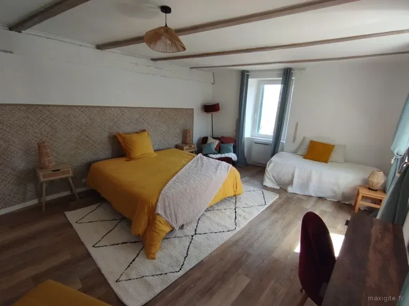 Chambre lumineuse sous poutres apparentes avec parure de lit jaune moutarde et coin salon
