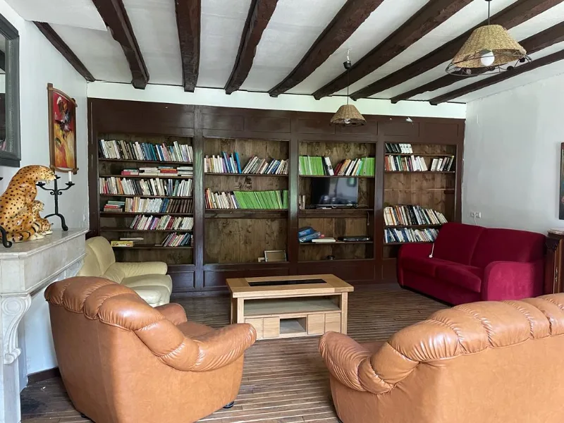 Salon-bibliothèque aux poutres apparentes avec cheminée en pierre et fauteuils en cuir
