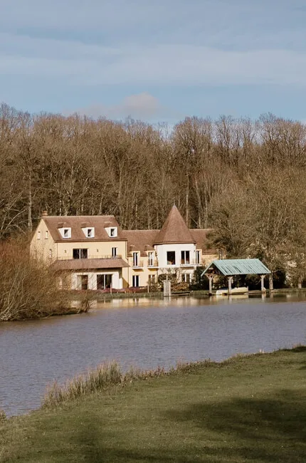 Gîte de groupe Domaine de Thironne à Montigny-le-Chartif — Façade du Manoir du Domaine de Thironne face au lac, arbres nus en hiver, capacité 39 personnes